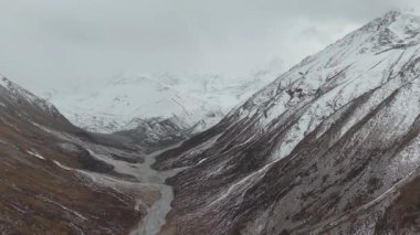 Hava manzarası derin bir vadide kıvrımlı bir nehri çevreleyen görkemli karlı dağları yakalar, doğal güzelliği ve engebeli araziyi gözler önüne serer, geniş manzarayı gözler önüne serer.