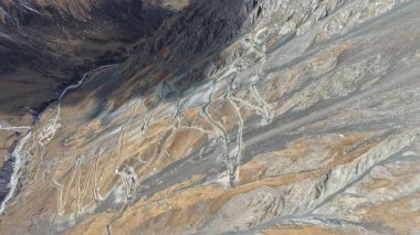 Büyüleyici hava perspektifi engebeli manzaralar ve vadilerle çevrili kayalık arazi boyunca uzanan dolambaçlı bir yolu gösteriyor. Bölgenin doğal güzelliğini ve macerasını vurguluyor.