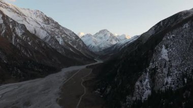 Gökyüzü perspektifi karlı dağları yakalıyor. Sakin bir vadide kıvrımlı bir nehri çerçeveliyor. Görkemli manzarayı ve doğal güzelliği gözler önüne seriyor.
