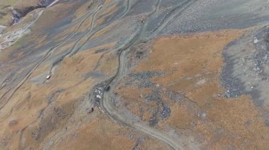 Hava perspektifi virajlı bir yol ile engebeli araziyi yakalar, doğal güzelliği ve manzaranın dokusunu gözler önüne serer, kamera sahne boyunca düzgün bir şekilde hareket eder.