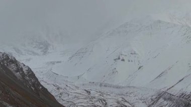Karlı dağ manzarası, engebeli arazinin karmaşık dokularını ve şablonlarını gözler önüne seriyor. Kamera giderek yaklaşarak kar ve kaya oluşumlarının dramatik zıtlıklarını gösteriyor.