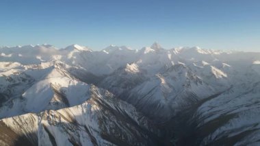 Karla kaplı dağ sırası panoramasında görkemli tepeler ve vadiler sergilenirken, genişleyen manzarayı ve berrak mavi gökyüzünü gösteren kademeli bir zoom doğal güzellik ve dinginliği vurguluyor.