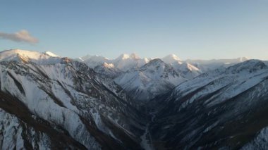 Hava görüntüsü karla kaplı dağları yakalar, ihtişamını ve dokusunu gözler önüne serer, kamera giderek yaklaşırken, manzaranın karmaşık detaylarını gözler önüne serer.
