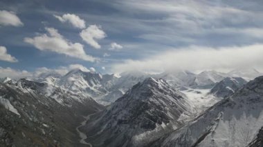 Görkemli dağ manzaraları, karlı tepeler ve dalgalı vadileri gösteriyor. Kamera, dinamik bulut hareketini ve doğanın enginliğini yakalıyor.