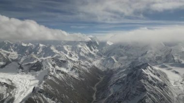 Hava perspektifi, karla kaplı dağların nefes kesen genişliğini yakalar, kayan bulutları ve engebeli araziyi gösterir, kamera çarpıcı manzarada pürüzsüz bir şekilde hareket eder.