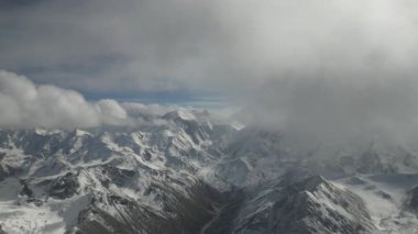 Karlı dağ manzarası görkemli tepeleri ve dönen bulutları gözler önüne seriyor, kamera nefes kesici sahnede düzgün bir şekilde hareket ederken, çevrenin doğal güzelliğini gösteriyor.