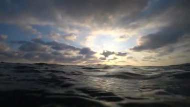 Güneş ışığıyla yıkanan, yumuşak, parlak enerjili okyanus dalgaları katmanlı bulutlu gökyüzünden süzülüyor ve doğal deniz manzarasını gösteren büyüleyici deniz manzarası yaratıyor.