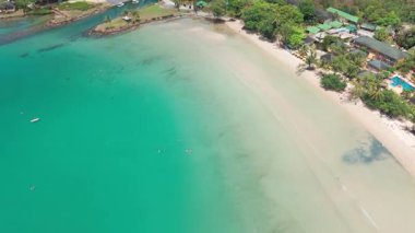 Turkuaz su, bereketli bitki örtüsüyle çevrili tropikal bir sahil beldesinin kumlu sahilinde nazikçe tur atar ve büyüleyici bungalovlar ve eğlence tesisleriyle noktalanır.