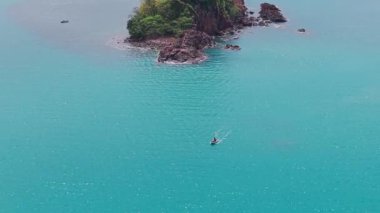 Kristal berrak turkuaz su, bereketli bitki örtüsüyle kaplı küçük, kayalık bir adanın çevresini sarar.
