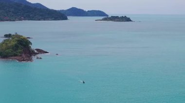 Kristal berrak turkuaz su, bereketli bitki örtüsüyle kaplı küçük, kayalık bir adanın çevresini sarar.