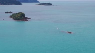 Kristal berrak turkuaz su, bereketli bitki örtüsüyle kaplı küçük, kayalık bir adanın çevresini sarar.