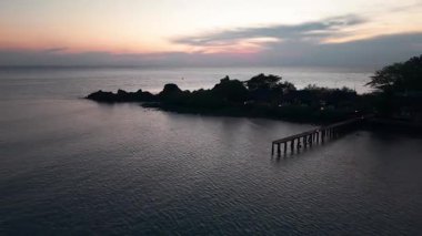 Sakin okyanus, tropikal bir plajın üzerindeki güzel günbatımında turistlerin yüzdüğü ve sıcak akşam atmosferinin tadını çıkardığı renkli gökyüzünü yansıtıyor.