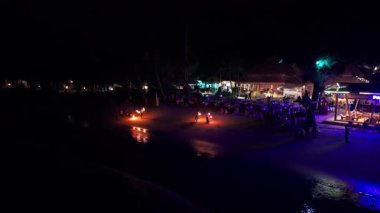 Gece vakti itfaiyeciler alevli aksesuarlar çeviriyor, büyüleyici dans hareketleri ve tropikal plaj zeminine karşı enerjik enerjisiyle otel misafirlerini eğlendiriyorlar.