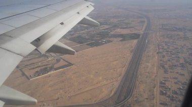 Uçak kanadı geniş bir çöl arazisi boyunca uzanır, yeşil alanlar ve yollar ağını ortaya çıkarır, kentsel gelişim ve doğal arazi arasındaki zıtlığı gözler önüne serer.