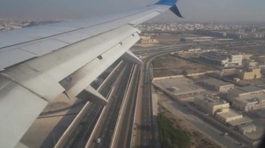 Abu Dabi, BAE - 18 Ocak 2026: Arka planda kentsel yapılar ve yer işaretleri olan uçak kanatları, iniş noktasından piste geçerek bir şehir manzarasına doğru genişliyor.