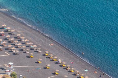 Kamari, Santorini Adası, Yunanistan - 19 Eylül 2020: Kamari tatil beldesinde siyah, volkanik plaj esprili sandalyeler. Ege Kıyı Denizi.