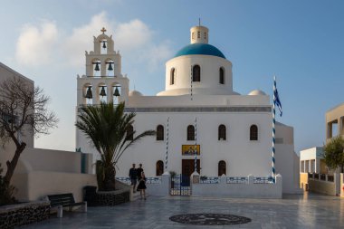 Oia, Santorini Adası, Yunanistan - 18 Eylül 2020: Panagia Platsani Ortodoks Kilisesi Oia 'nın tepedeki köyünde bir Yunan bayrağı dalgalanıyor.