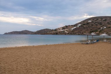 Yunan adası Ios 'ta güneşli yataklar ve şemsiyelerle kumlu bir sahil manzarası. Bulutlu bir gün.