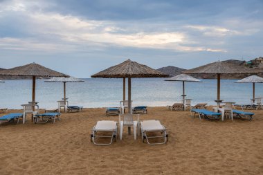 Yunan adası Ios 'ta güneşli yataklar ve şemsiyelerle kumlu bir sahil manzarası. Bulutlu bir gün.