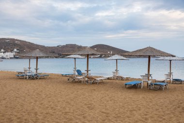 Yunan adası Ios 'ta güneşli yataklar ve şemsiyelerle kumlu bir sahil manzarası. Bulutlu bir gün.