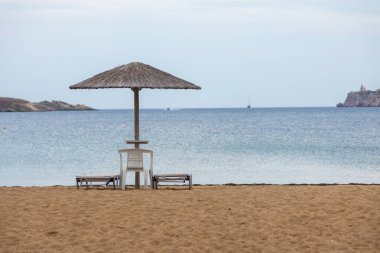 Yunan adası Ios 'ta güneşli yataklar ve şemsiyelerle kumlu bir sahil manzarası. Bulutlu bir gün.
