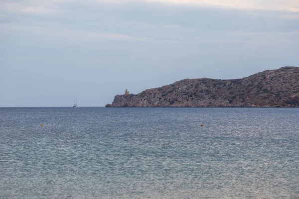 View of the lighthouse on the peninsula. A boat running on the bay, Paralia Gialos, Ios Island, Greece.