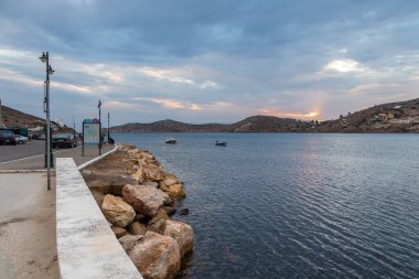 Paralia Gialos, Ios Adası, Yunanistan... 19 Eylül 2020, körfeze demir atmış tekne. Limanda, otoparkta, arabalarla. Tepelerde gün batımı.