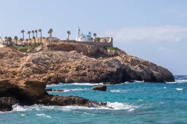 Ios adasının güney kıyısında kayalık bir sahil. Arka planda beyaz, geleneksel bir Yunan kilisesi. Yunanistan.