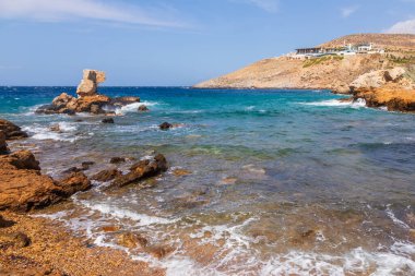 Ios adasının kuzey kıyısında kayalık bir sahil. Arka planda beyaz, geleneksel bir restoran binası. Yunanistan.