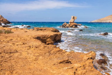 Ios adasının kuzeyinde kayalık kıyı zekası karakteristik oluşumu. Sahilde renkli tekneler. Arka planda beyaz, geleneksel bir Yunan kilisesi. Yunanistan.