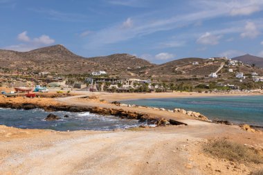 Kuzey Ios Adası, Yunanistan - 20 Eylül 2020: Tatil köyünde Rocky Sahili. Sahilde renkli tekneler. Beyaz, geleneksel bir restoran binası..