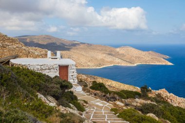Palaiokastro Kalesi 'nin yanındaki küçük taş binanın manzarası. Ayırt edici beyaz eklemli taş yol. Arka planda kıyı var. Ios Adası, Yunanistan.