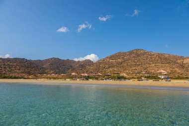 Ios Adası, Yunanistan - 21 Eylül 2020: Ios adasındaki turkuaz sularıyla popüler Manganari plajına bakın. İnsanlar güneş pansiyonlarında güneşleniyor..