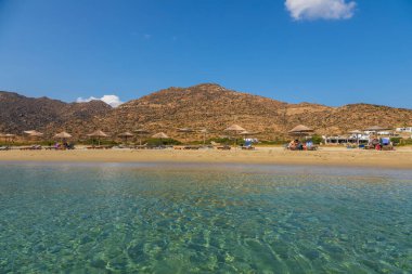 Ios Adası, Yunanistan - 21 Eylül 2020: Ios adasındaki turkuaz sularıyla popüler Manganari plajına bakın. İnsanlar güneş pansiyonlarında güneşleniyor..