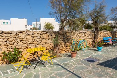 Renkli mobilyalar, masa, sandalyeler ve bisiklet. Yerel restoranın dekoru. Arka planda taş duvar var. Folegandros Adası, Yunanistan.