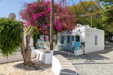 Folegandros Adası, Chora, Yunanistan - 23 Eylül 2020: Yerel restoranları olan ana meydanın manzarası. Misafirler için masaların dışında. Çiçekli pembe bugenwilla.