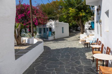 Folegandros Adası, Chora, Yunanistan - 23 Eylül 2020: Yerel restoranları olan ana meydanın manzarası. Misafirler için masaların dışında. Çiçekli pembe bugenwilla.