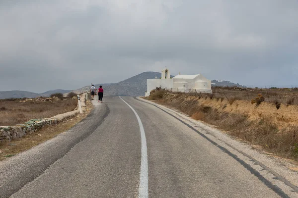 Stock image Folegandros Island, Greece - 24 September 2020: Traditional white chapel, a small church by the road. People on a walk.