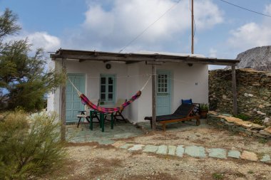 Folegandros Adası 'ndaki popüler tatil köyündeki küçük beyaz evin manzarası. Binanın önündeki hamak ve güverte sandalyesi. Cyclades Archipelago, Yunanistan.