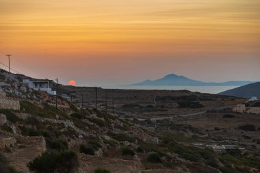 Chora 'nın üzerinde gün batımı. Geleneksel Yunan binaları ve sahil manzarası. Folegandros Adası, Yunanistan.