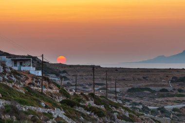 Chora 'nın üzerinde gün batımı. Geleneksel Yunan binaları ve sahil manzarası. Folegandros Adası, Yunanistan.