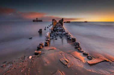 Denizde kış manzarası. Baltık Denizi 'ndeki 2. Dünya Savaşı torpido platformuna giden donmuş ahşap dalgalar. Polonya, Babie Doly 'de sabah. Uzun pozlama fotoğrafı. Güzel gün doğumu.