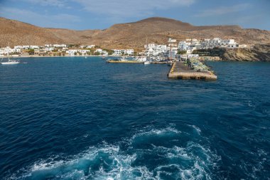 Folegandros Adası, Yunanistan - 26 Eylül 2020: Ege Denizi 'nde uyanma büyük bir gemi tarafından yapıldı. Arka planda geleneksel binalar olan liman.