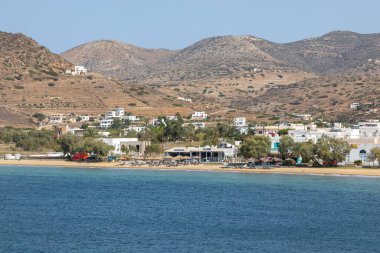 Chora, Ios Adası, Yunanistan - 26 Eylül 2020: Yunanistan 'ın Ios adasındaki güneşlik ve şemsiyelerin kumlu sahili. Arka planda kasaba. Bulutlu bir gün.