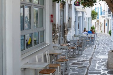 Parikia, Paros Adası, Yunanistan - 26 Eylül 2020: Eski şehrin dar sokakları. Geleneksel, geniş mimari ve beyaz eklemli taş bir yol. Yerel restoranlarda masalarda oturan insanlar.