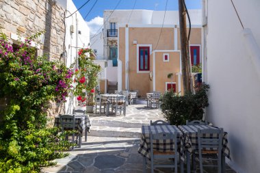 Naoussa, Paros Adası, Yunanistan - 27 Eylül 2020: Yerel restoranı ve dükkanları olan dar balıkçı köyü manzarası. Misafirler için masaların dışında. Çiçekli ağaç.