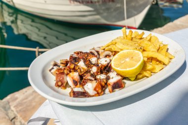 Beyaz tabakta taze ahtapot ve limon ve patates kızartması. Geleneksel Akdeniz yemeği, Naoussa 'daki Taverna, Paros Adası, Yunanistan.