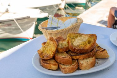 Beyaz tabakta ızgara buğday ekmeği, otlar ve zeytinyağı. Geleneksel Yunan mezeleri. Naoussa, Paros Adası, Yunanistan.