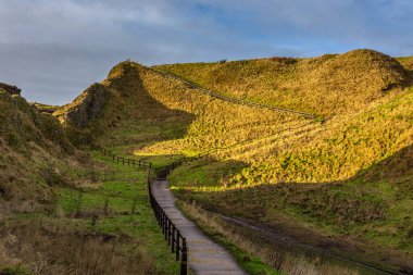 Yeşil tepeler arasındaki Dunnottar Şatosu 'na giden yolun manzarası. Güneşli güzel bir sabah. Stonehaven, Aberdeenshire, İskoçya, Birleşik Krallık.