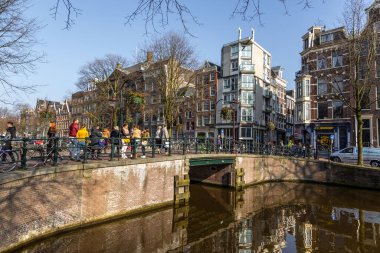 Amsterdam, Hollanda - 12 Mart 2016: Amstel Kanalı 'ndaki tekneler ve etrafta dolaşan insanlar. Amstel Kanalı üzerindeki köprü. Tipik Hollandalı evleri. Şehir görünümü.